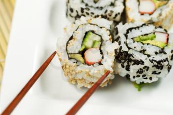Closeup horizontal photo of a single inside out California roll being picked up with chopsticks   