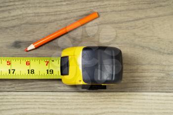 Horizontal photo of open tape measure and orange pencil on aged wood  