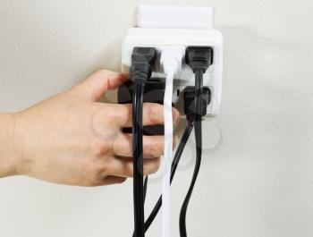 Photo of female hand plugging in power adapter into multiple electrical wall unit outlets
