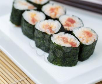 Closeup photo of freshly made spicy tuna sushi roll in white plate and chop sticks in background with bamboo mat underneath 