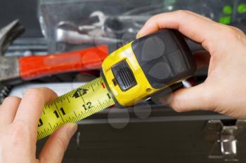 Horizontal photo of female hands pulling used tape measure out with old toolbox in background 