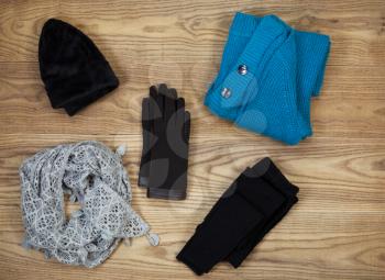 Overhead view of fall or winter clothing and accessories placed on rustic wooden boards.  Items include gloves, hat, wool socks, scarf, and sweater. 