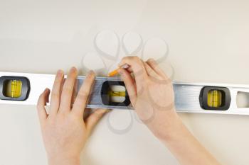 Horizontal photo of female hands using level and pencil on interior white wall
