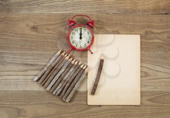 Overhead view of old pencils with tree bark, aged paper and alarm clock on rustic wood