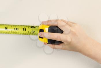 Horizontal photo of female hands using tape measure on interior home white wall