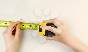 Horizontal photo of female hands using tape measure and pencil on interior home white wall