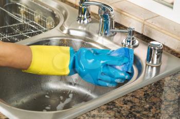 Closeup horizontal image of hand wearing rubber glove washing inside of kitchen sink with sponge and soapy water 