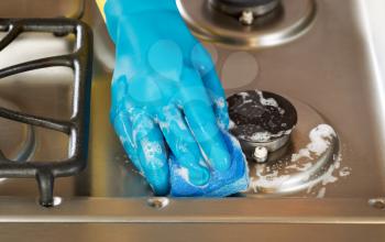 Closeup horizontal image of hand wearing rubber glove while cleaning stove top range with soapy sponge 