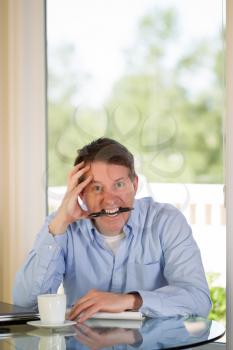 Vertical image of mature man showing extreme stress, looking forward, while working from home with bright daylight coming in from window in background