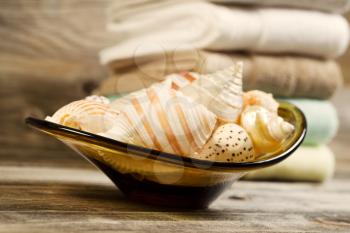 Horizontal eye level view of seashells in glass bowl with clean stacked towels in background on rustic wood