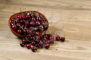 Horizontal view of fresh black cherries spilling out of basket onto rustic wooded boards