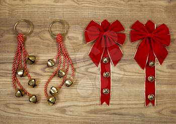 Overhead view of Christmas red bows and rope with golden bells positioned on rustic wooden boards.  

