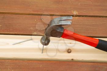 Horizontal photo of used hammer pounding nailing into new boards for installing on cedar deck