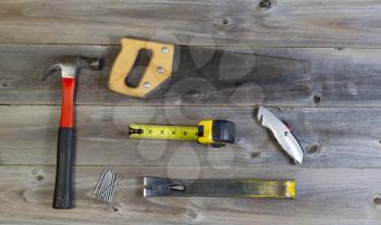 Top view of basic home repair tools consisting of wood saw, hammer, nails, box cutter, pry bar and tape measure on rustic wooden boards