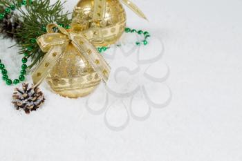 Closeup front view of golden Christmas Ornament with snow covered branch and pine cones in background 
