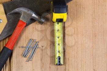 Top view of home repair tools consisting of wood saw, hammer, nails, and tape measure on cedar wooden shingles for roof