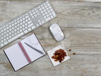 Top view of business office consisting of computer keyboard, notepad, pen, and snack food on rustic white wooden desktop 
