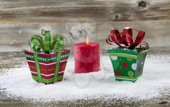 Vibrant packaged gifts and glowing red candle for the holiday season on rustic wood with snow