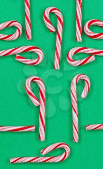 Top view vertical orientation shot of red and white stripped Christmas candy canes on a solid green background. Random patterns with canes in and out of the frame. 