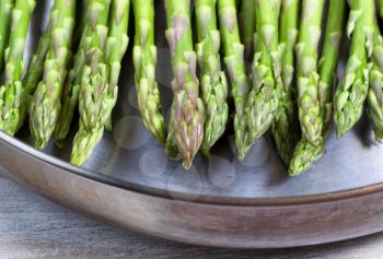 Close up view of a fresh asparagus, focus on front part with shallow depth of field, in stainless steel fry pan on wood 