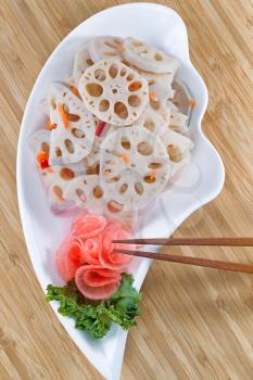 Top view vertical image of Chinese lotus water radish, in white dish, with chopsticks on natural bamboo background 