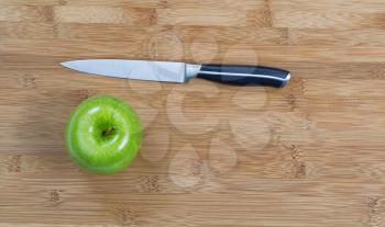 Top view of whole green apple and cutting knife on natural bamboo board