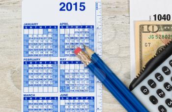 U.S. Tax form 1040 with calculator, calendar, currency and pencils on wooden desktop 
