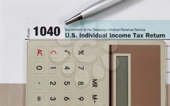 Close up of income tax form, silver pen and calculator with gray folder underneath. Business financial concept. 