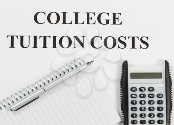 Overhead view of white paper with wording of college tuition costs along with silver pen, calculator, and notebook. 