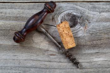 Top view angled shot of vintage corkscrew with single used cork on rustic wooden boards