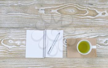 Top view shot of an old white desktop with notepad, pen and green tea in cup in horizontal format with plenty of copy space. 