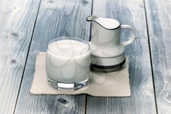 Vintage concept of a  glass of milk and pitcher on rustic wood


