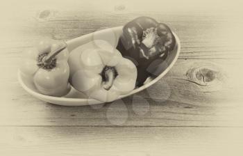 Vintage concept of three fresh bell peppers in white bowl on aged wood