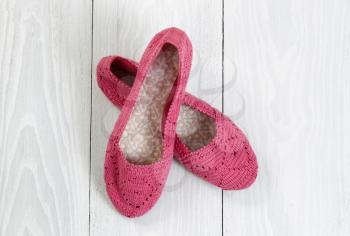 Knitted pink shoes on white wood boards. 