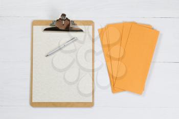 Clipboard with paper, pen and envelopes on white desktop.