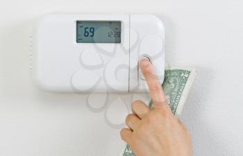 Close up of female hand adjusting home heating thermostat with partial currency money in palm. 