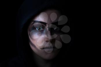 Teen girl wearing hoodie with scary face makeup on black background. 