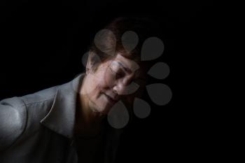 Senior woman bending forward while displaying pain on black background.