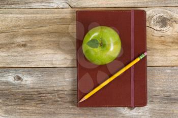 Top view of green apple, leather notepad and pencil on rustic wood.