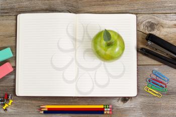 Top view of green apple, open notepad surrounded with supplies on rustic wood.