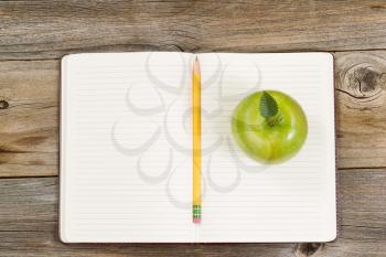 Top view of green apple, open notepad with pencil in center on rustic wood.