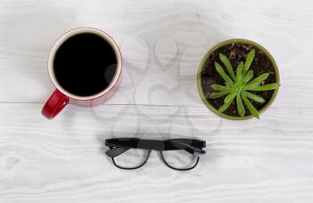 White desktop with red coffee cup, reading glasses, and baby plant
