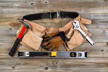 Traditional leather tool belt with tools on rustic wooden floor.