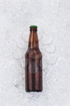 Single bottle of beer cooling down on pile of ice. Layout in vertical format. 