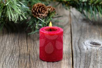 Single red candle with flame and evergreen setting on rustic wood. Selective focus on front part of candle and flame.   
