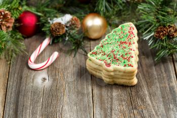 Close up view of tree shaped cookies with evergreen branches, pine cones, snow and ornaments on rustic wood. Selective focus on upper part of cookies. 