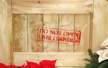 Close up of wooden box with red text stating do not open until Christmas. Partial poinsettia and evergreen.