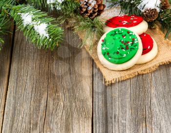 Colorful cookies with snow covered evergreen branches, and pine cones on rustic wood. 