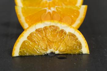 Close up of a juicy slice of orange fruit on natural slate stone. Selective focus on front part of fruit. 