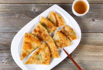 Top view of fried Asian pancakes with green tea and chopsticks on white plate. Rustic wooden boards underneath. 